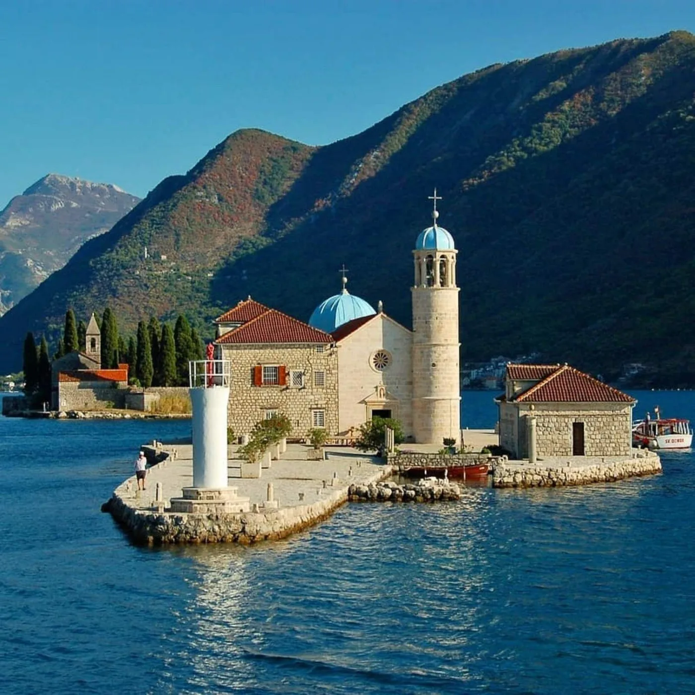 The island church of Our Lady of the Rocks with its blue dome and bell tower, set on the water below the steep green mountains of the Bay of Kotor