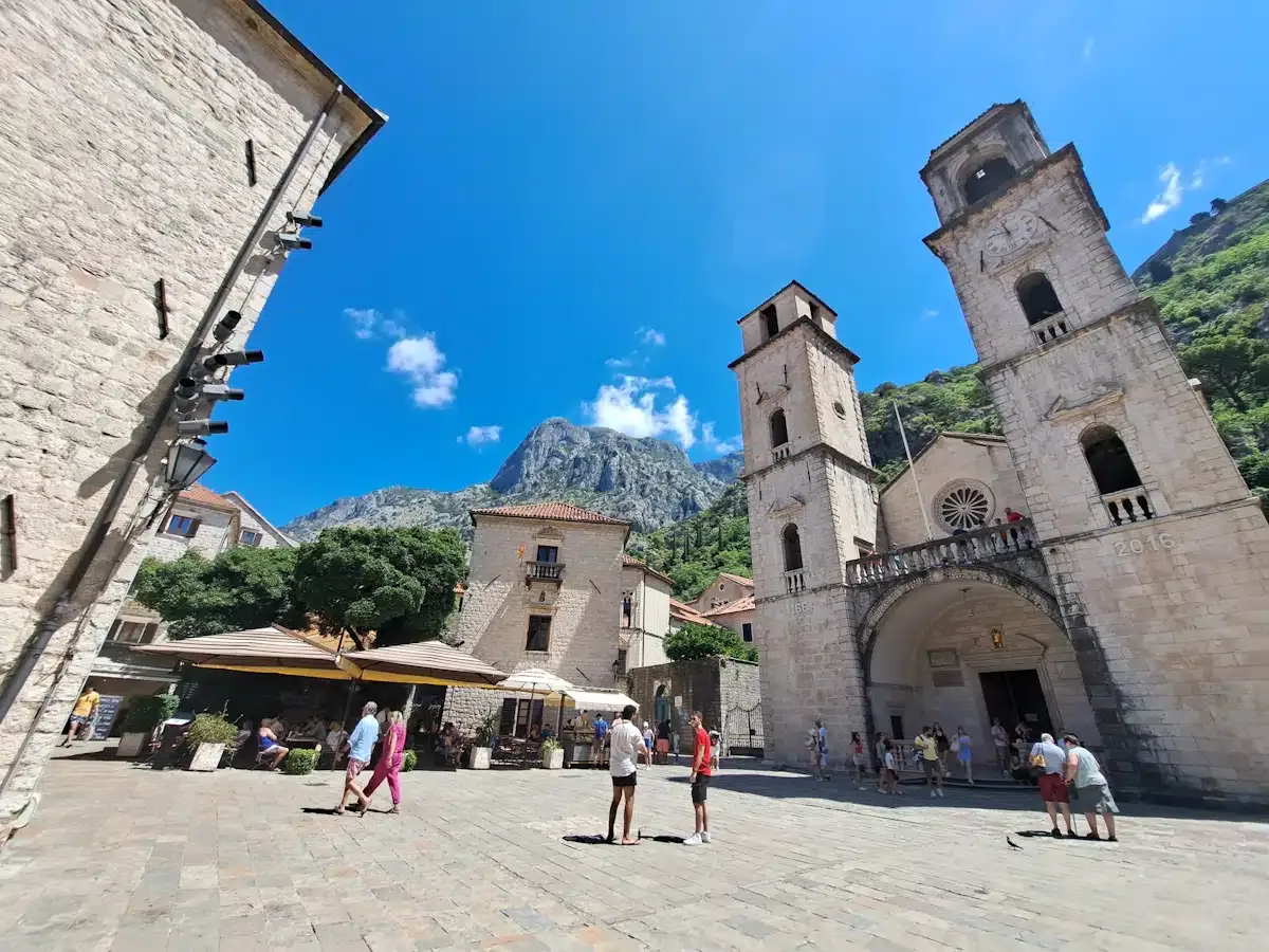 St Tryphon Cathedral and its square in Kotor Old Town, with the bare mountain ridge rising directly behind the stone bell towers